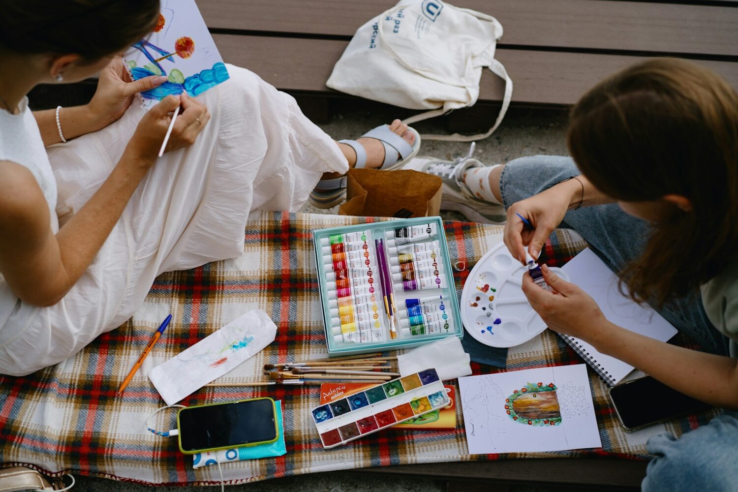 Two people sitting on a blanket painting pictures