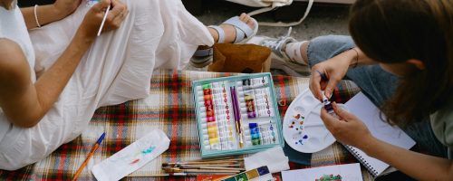 Two people sitting on a blanket painting pictures